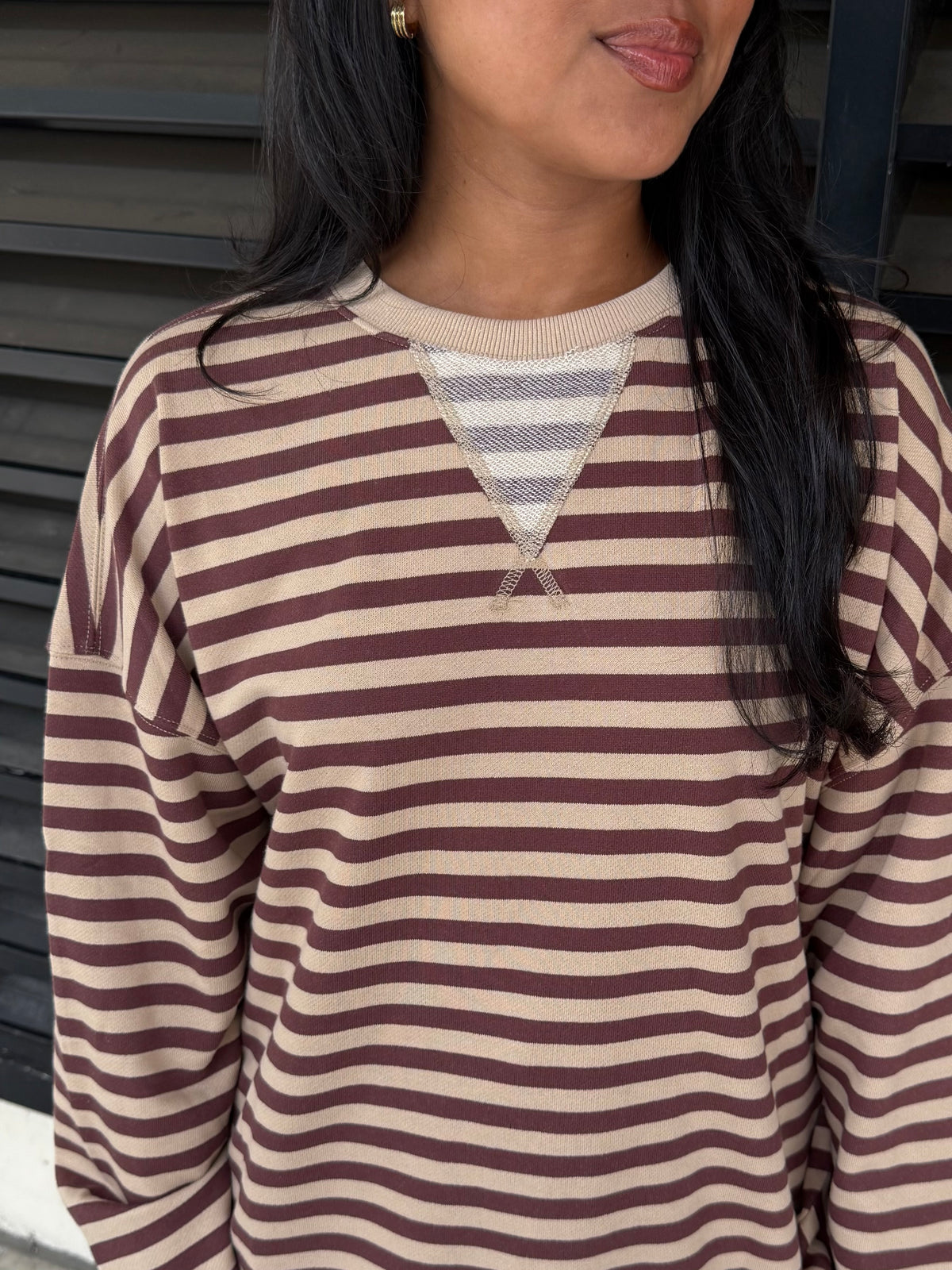 A close-up of a person wearing a long-sleeve knit top with horizontal brown and beige stripes and a V-shaped neckline detail.