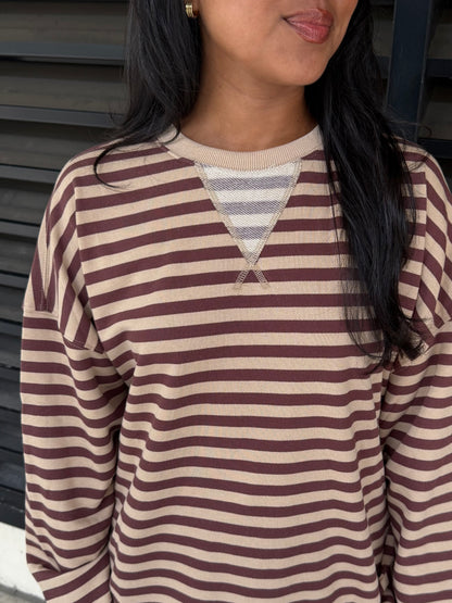 A close-up of a person wearing a long-sleeve knit top with horizontal brown and beige stripes and a V-shaped neckline detail.