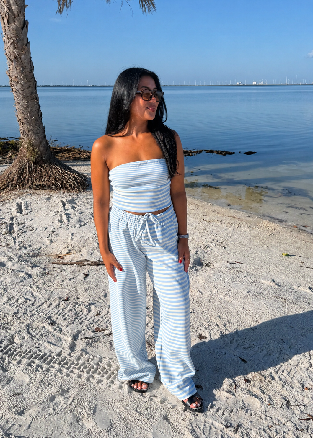 woman wearing striped top and striped pants on sand and water background