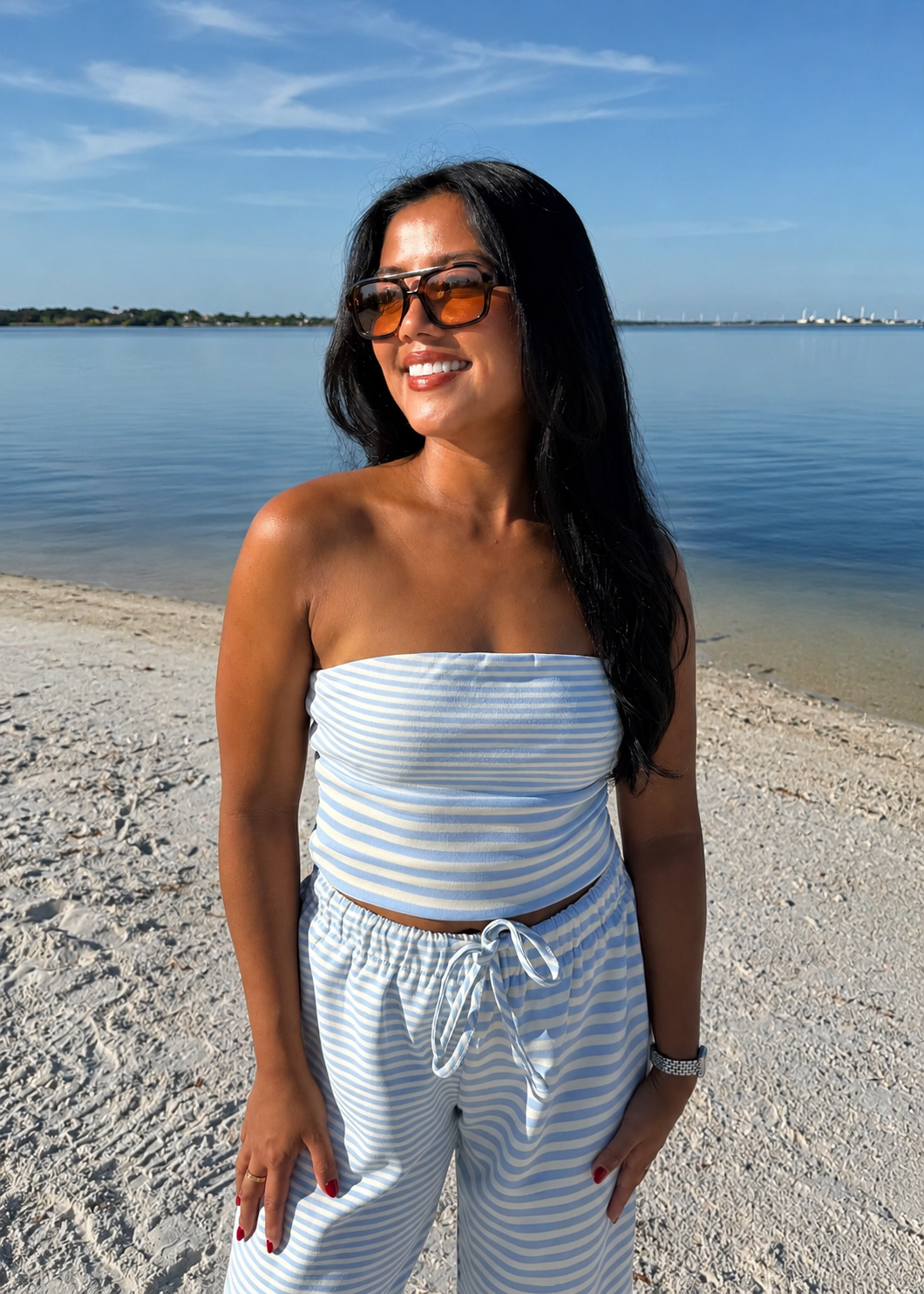 woman wearing striped top and striped pants on sand and water background