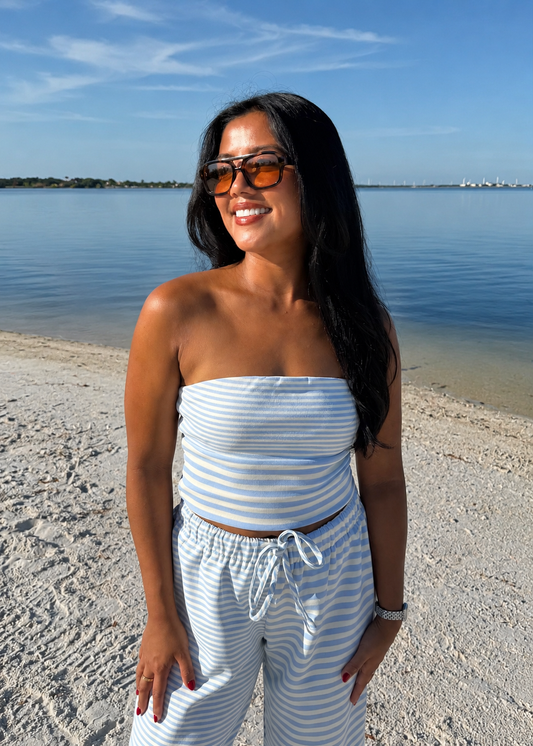 woman wearing striped top and striped pants on sand and water background