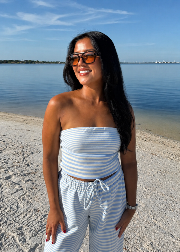 woman wearing striped top and striped pants on sand and water background